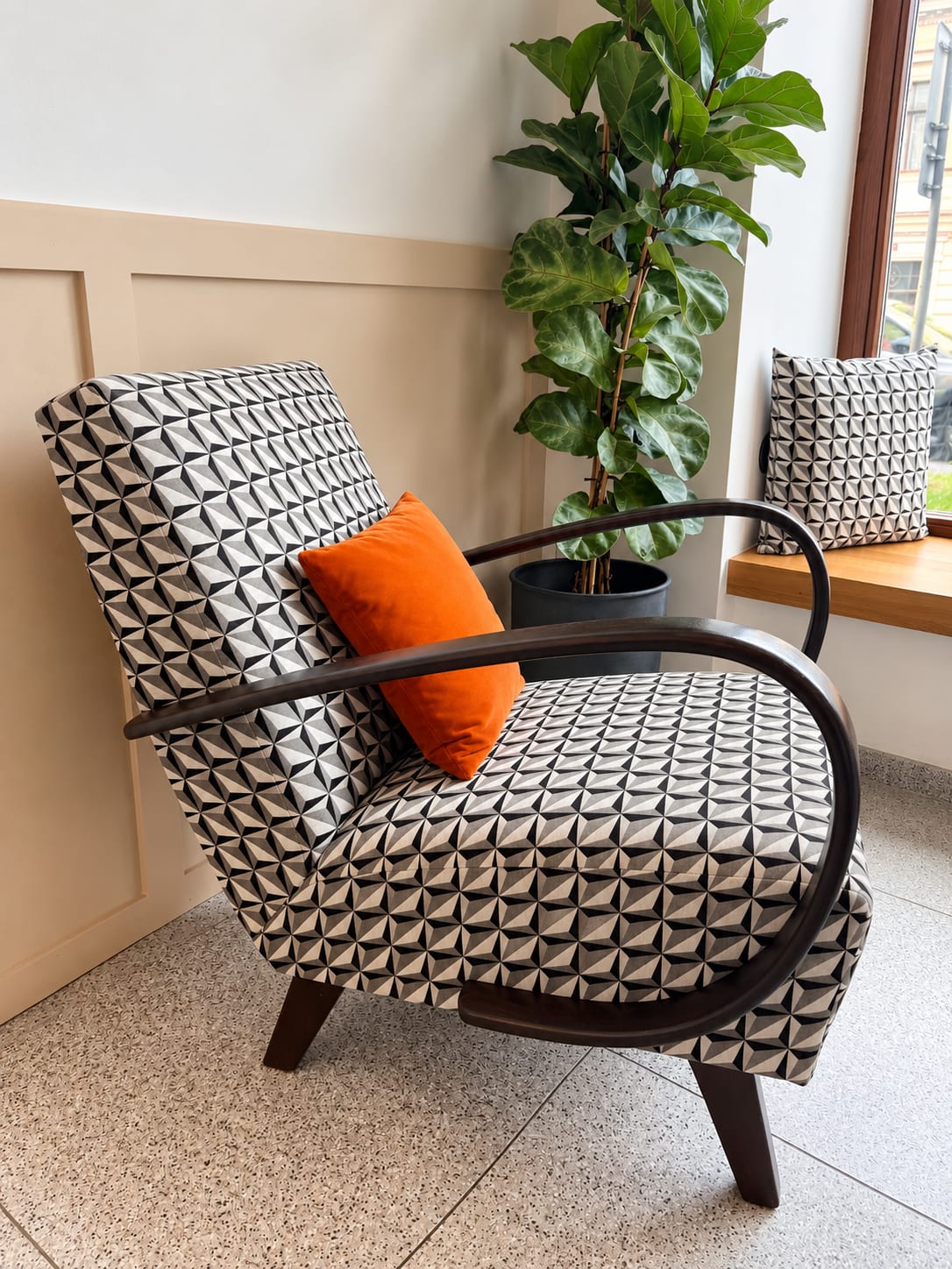 Retro křeslo Jindřicha Halabaly s novým černobílým geometrickým čalouněním a oranžovým polštářem
